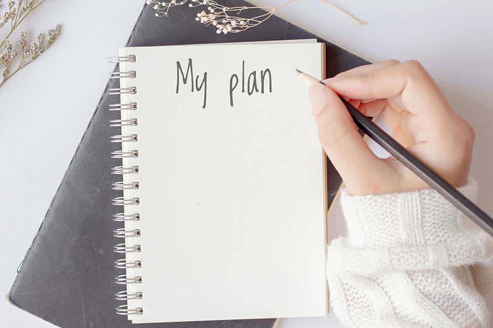 Woman hand holding pencil with the notebook with My Plan text is on top of white notebook on office desk table.