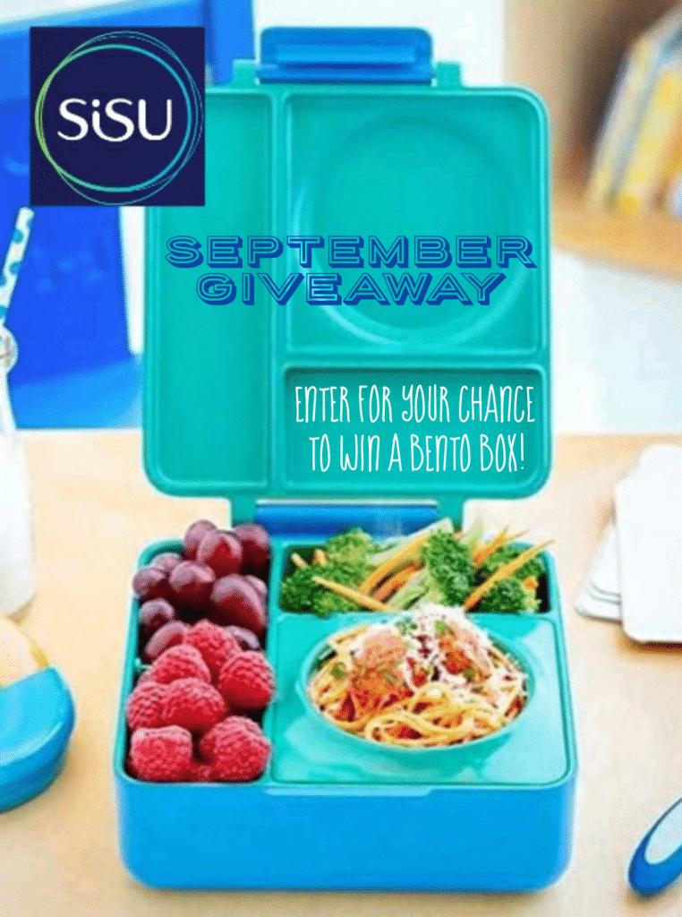 A blue bento box with berries and grapes in the left side smaller compartments and broccoli with carrots in the top compartment and spaghetti and meatballs in the main compartment. The bento box is on a wooden table top with miscellaneous items on it. In the background, you can see a blue chair, a bookshelf and part of the floor. The caption reads "Sisu September Giveaway - Enter for your chance to win a bento box!"